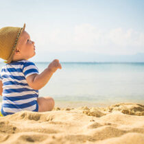The cute baby boy playing on the beach. Little boy sitting on the sand. Sea and seashore as background with copy space