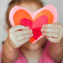 DIY holiday card with a red paper heart, a symbol of love. child holding homemade paper cut hearts Mother's Day, Valentine's Day
