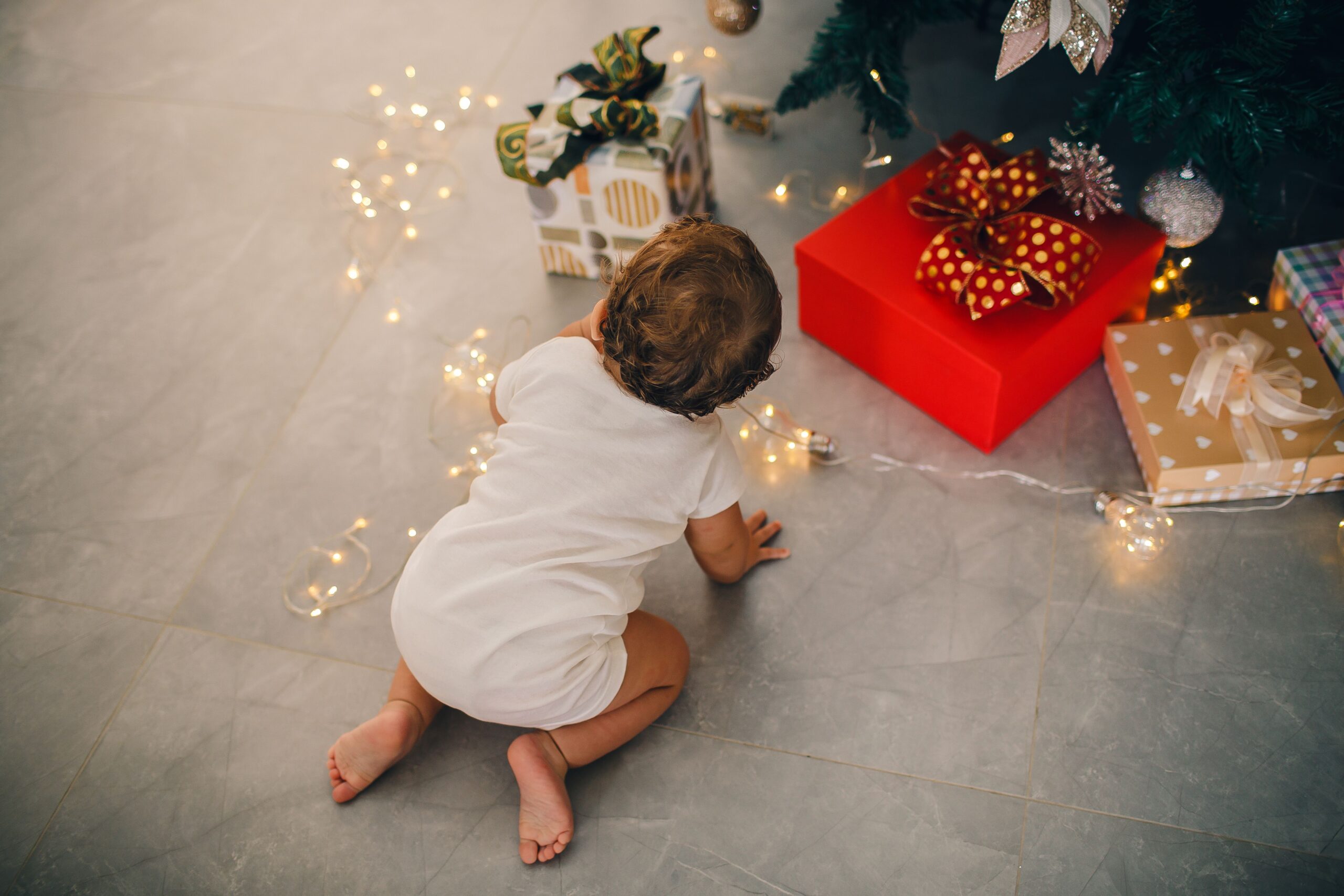 Bébé à quatre pattes devant le sapin et les cadeaux pour son premier Noël